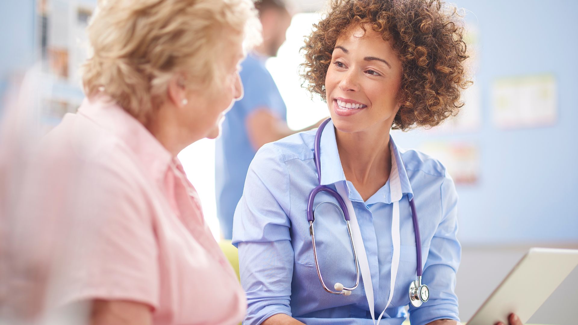 A doctor speaks with a woman wearing a hospital gown, discussing her health.