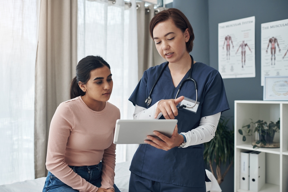 A female doctor consults with a patient via a tablet, discussing health matters in a virtual setting.