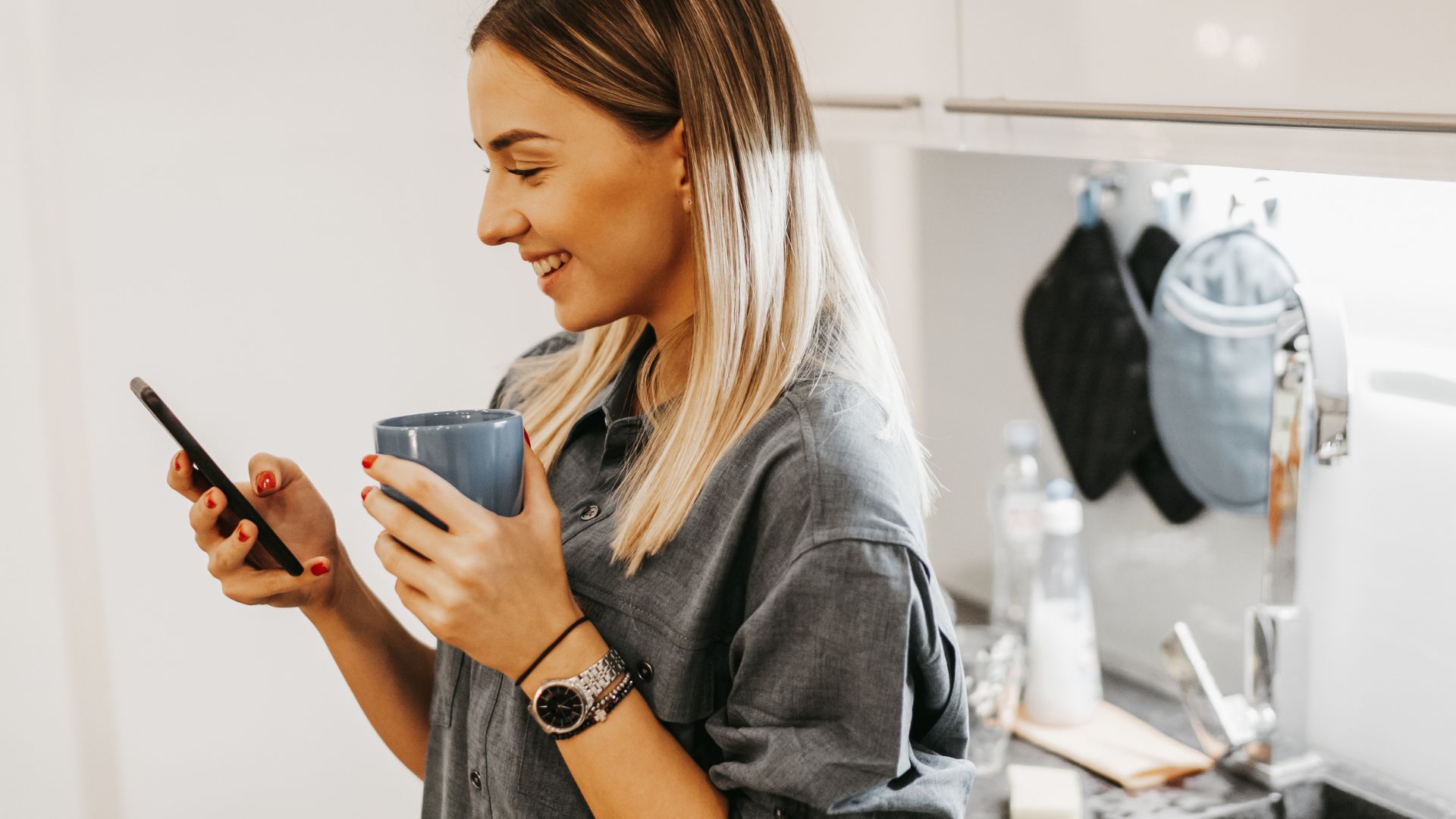 A woman holding a cup while looking at her phone, appearing focused and engaged in her device.